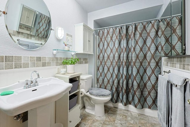 bathroom with stone finish flooring, a wainscoted wall, a sink, and toilet