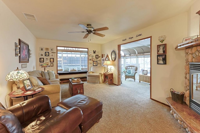 carpeted living room featuring ceiling fan, visible vents, a wealth of natural light, and a stone fireplace