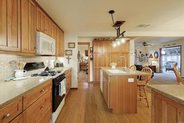 kitchen featuring white microwave, a kitchen island with sink, a kitchen breakfast bar, hanging light fixtures, and gas range