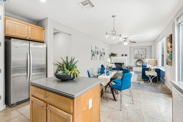 kitchen featuring a kitchen island, stainless steel fridge, light tile patterned floors, ceiling fan, and a brick fireplace