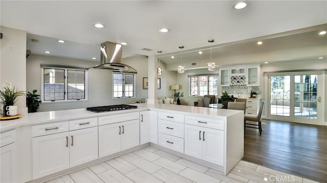 kitchen featuring white cabinetry, island range hood, kitchen peninsula, and stainless steel gas cooktop