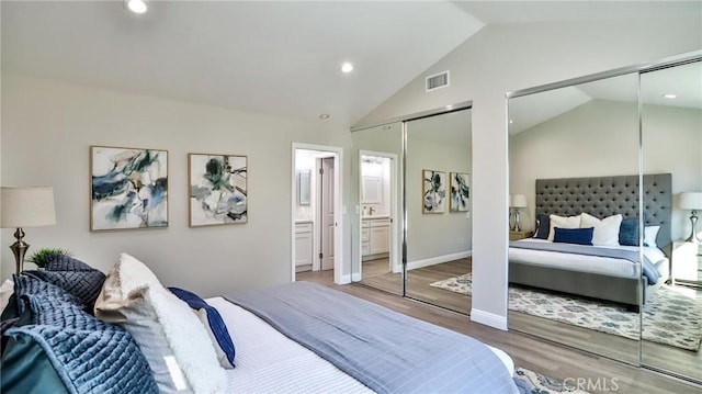 bedroom featuring multiple closets, vaulted ceiling, hardwood / wood-style floors, and ensuite bathroom