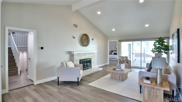 living room featuring beamed ceiling, high vaulted ceiling, a stone fireplace, and light hardwood / wood-style floors