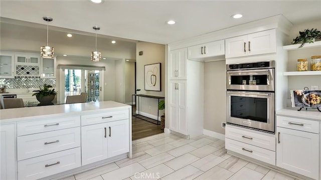 kitchen with white cabinetry, double oven, decorative light fixtures, and tasteful backsplash