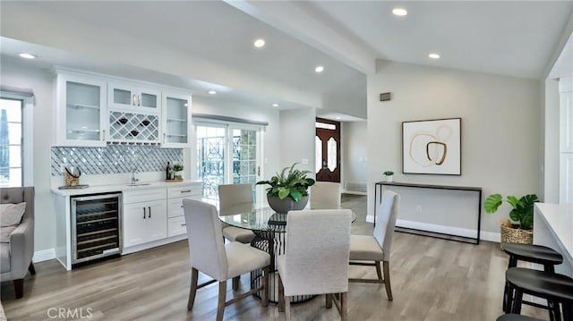 dining room featuring wine cooler, light hardwood / wood-style flooring, lofted ceiling with beams, and wet bar