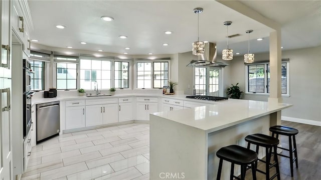 kitchen with sink, white cabinetry, island range hood, decorative light fixtures, and stainless steel appliances