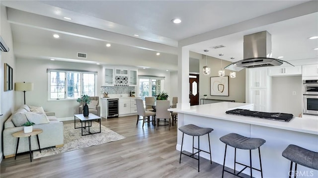 kitchen featuring pendant lighting, a breakfast bar, stainless steel appliances, white cabinets, and island exhaust hood