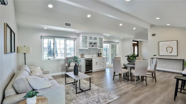 living room featuring vaulted ceiling with beams, a wealth of natural light, light hardwood / wood-style floors, and bar area