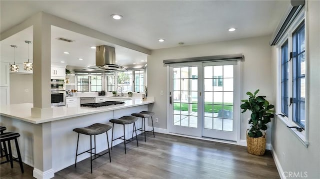 kitchen featuring a breakfast bar, island range hood, kitchen peninsula, and white cabinets