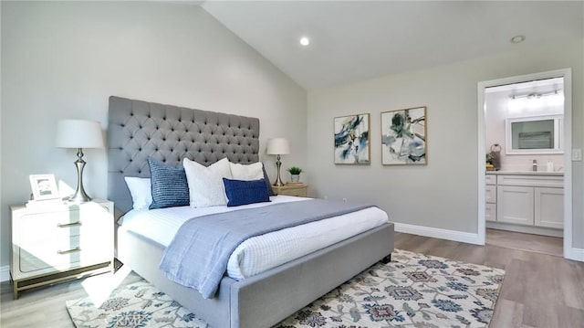 bedroom with ensuite bathroom, vaulted ceiling, and light wood-type flooring