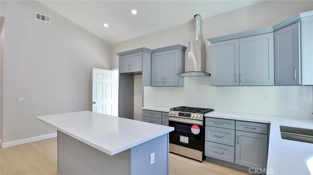 kitchen with gray cabinets, stainless steel gas stove, a center island, wall chimney range hood, and light wood-type flooring