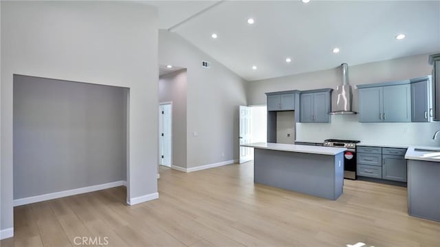 kitchen with gas range, high vaulted ceiling, light hardwood / wood-style flooring, a kitchen island, and wall chimney range hood