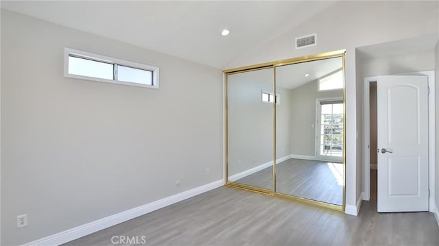 unfurnished bedroom featuring lofted ceiling, hardwood / wood-style floors, and a closet