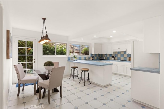 kitchen with a breakfast bar, white cabinetry, hanging light fixtures, kitchen peninsula, and decorative backsplash