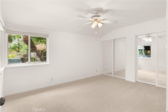 unfurnished bedroom featuring ceiling fan, light carpet, and two closets