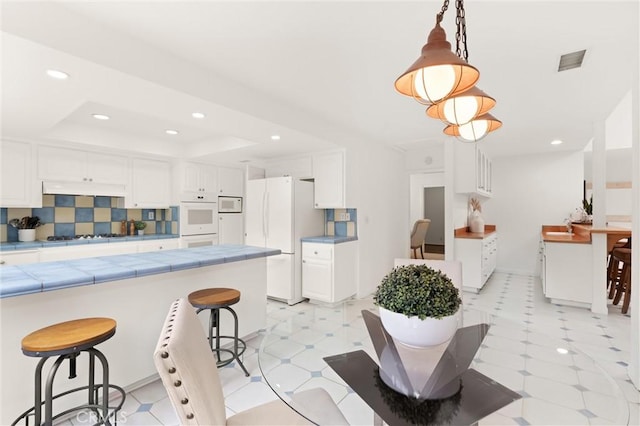 kitchen with pendant lighting, white appliances, a breakfast bar, tasteful backsplash, and white cabinets