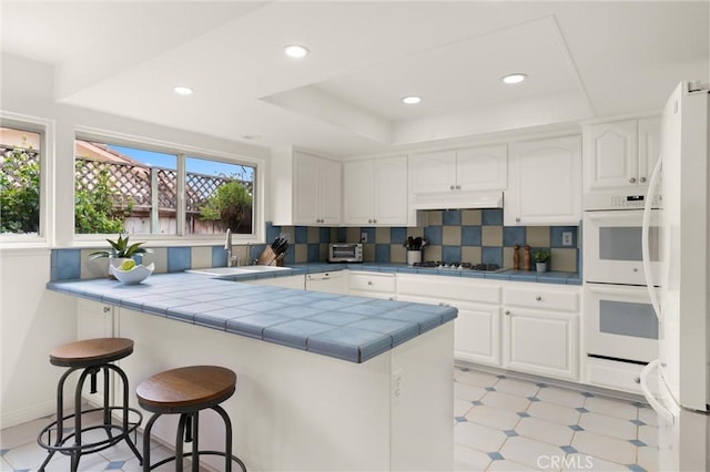 kitchen with sink, white cabinetry, a tray ceiling, tile countertops, and kitchen peninsula