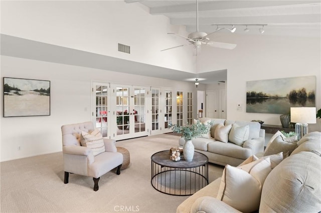 living room with rail lighting, ceiling fan, beam ceiling, light carpet, and french doors