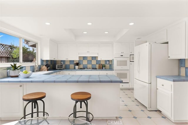 kitchen featuring white cabinetry, sink, a breakfast bar area, kitchen peninsula, and white appliances