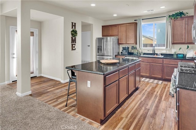 kitchen with sink, a center island, light hardwood / wood-style flooring, stainless steel fridge, and dark stone counters