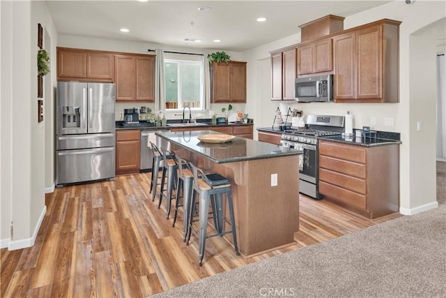 kitchen with sink, a breakfast bar area, appliances with stainless steel finishes, a center island, and light hardwood / wood-style floors