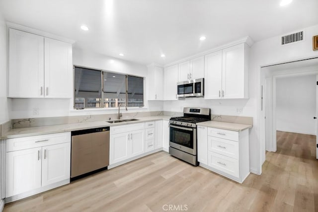 kitchen with light stone counters, stainless steel appliances, sink, and white cabinets