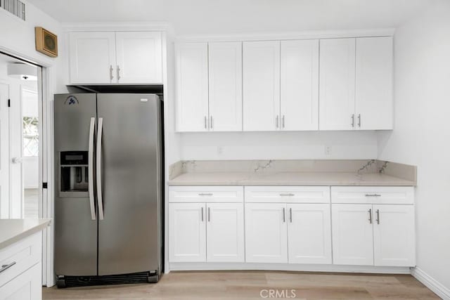 kitchen with stainless steel fridge, light stone countertops, white cabinets, and light wood-type flooring