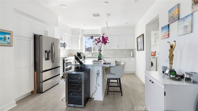 kitchen featuring appliances with stainless steel finishes, a kitchen island, washer / clothes dryer, white cabinetry, and wine cooler