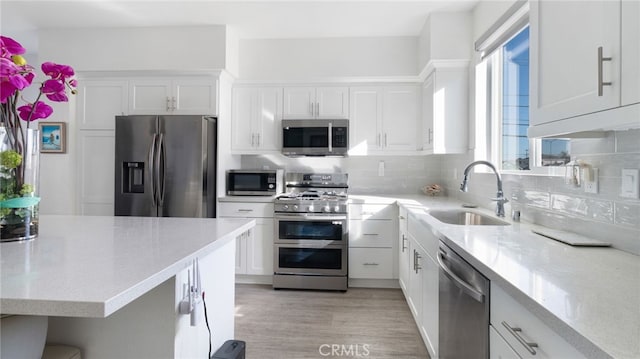 kitchen with sink, light hardwood / wood-style flooring, white cabinetry, backsplash, and stainless steel appliances