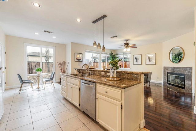 kitchen featuring sink, hanging light fixtures, dishwasher, an island with sink, and dark stone counters