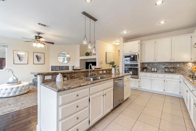 kitchen with sink, appliances with stainless steel finishes, hanging light fixtures, a center island with sink, and dark stone counters