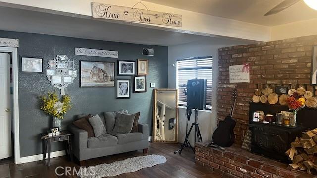 living room featuring a brick fireplace, dark wood-type flooring, and ceiling fan