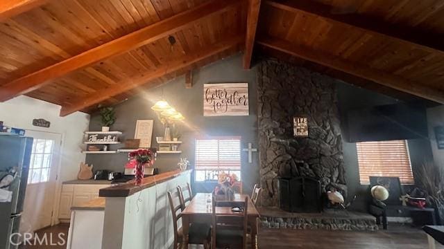 kitchen featuring a stone fireplace, white cabinetry, vaulted ceiling with beams, stainless steel fridge, and wooden ceiling