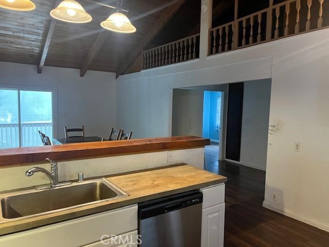 kitchen featuring stainless steel dishwasher, a sink, wooden counters, beam ceiling, and dark wood finished floors