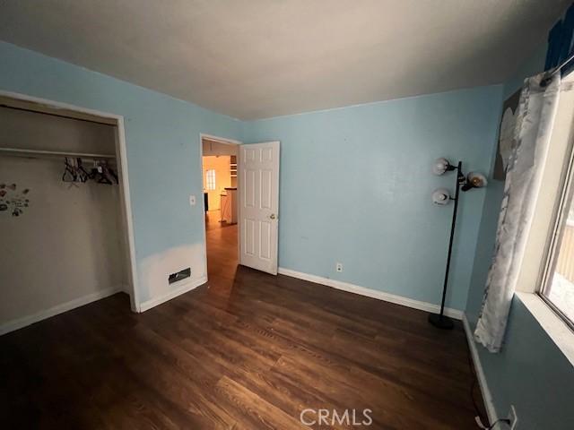 unfurnished bedroom featuring a closet, wood finished floors, and baseboards