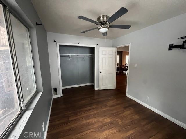 unfurnished bedroom featuring a closet, ceiling fan, wood finished floors, and baseboards