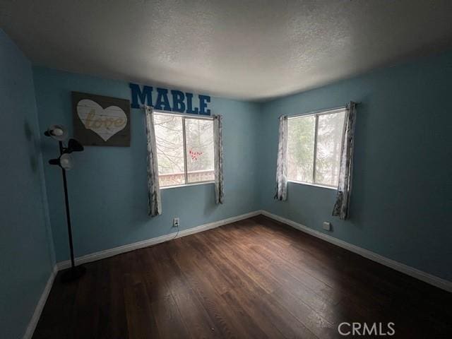 empty room featuring a textured ceiling, wood finished floors, and baseboards