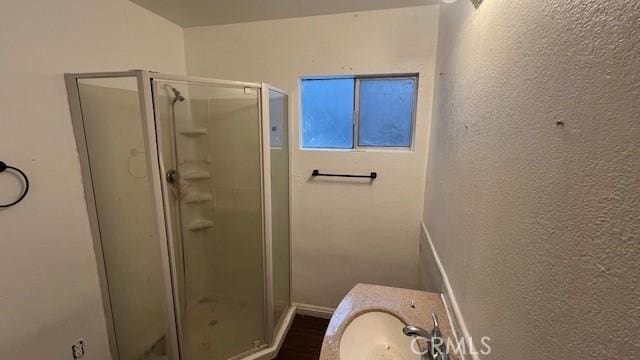 full bathroom featuring a textured wall, a shower stall, baseboards, and a sink
