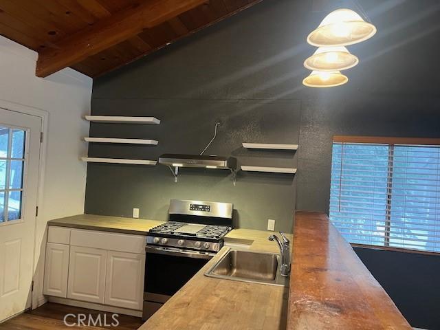 kitchen featuring open shelves, white cabinets, a sink, stainless steel gas range, and beam ceiling
