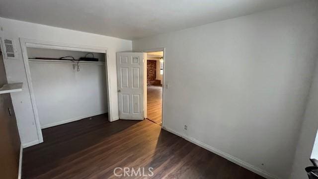unfurnished bedroom with wood finished floors, baseboards, visible vents, and a closet