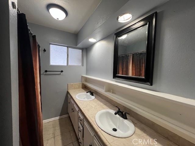 full bath with double vanity, tile patterned floors, baseboards, and a sink