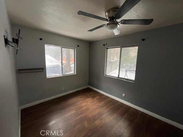 empty room with a textured ceiling, wood finished floors, ceiling fan, and baseboards