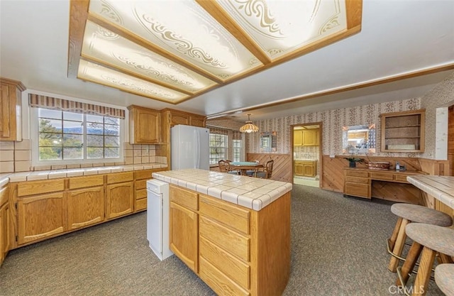 kitchen with plenty of natural light, hanging light fixtures, white refrigerator, and tile counters