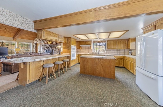 kitchen with white appliances, a center island, a kitchen breakfast bar, kitchen peninsula, and tile countertops