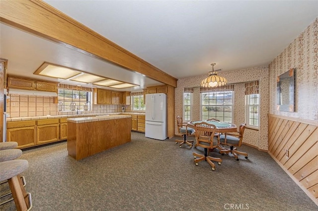 kitchen with beam ceiling, tile countertops, pendant lighting, white refrigerator, and a kitchen island