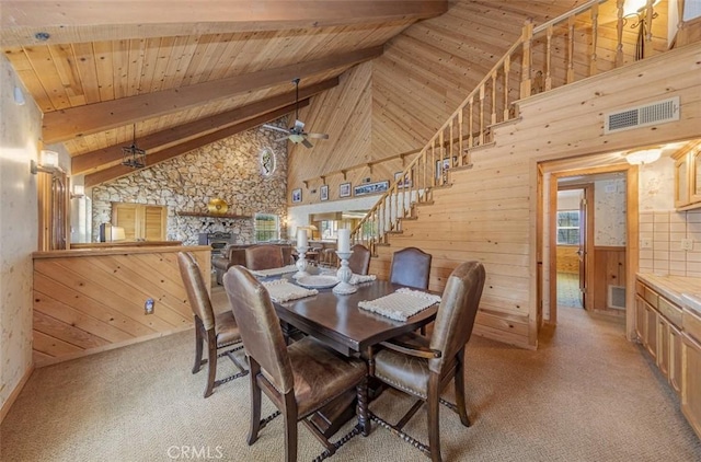 carpeted dining space featuring beam ceiling, ceiling fan, wood ceiling, and wooden walls