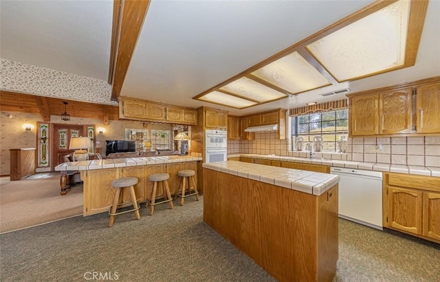 kitchen featuring tile countertops, white appliances, carpet floors, a breakfast bar, and a center island