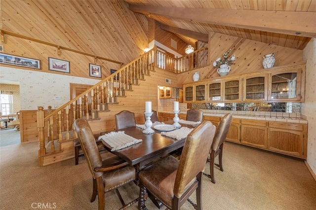 dining space with wood walls, beam ceiling, light carpet, and wooden ceiling