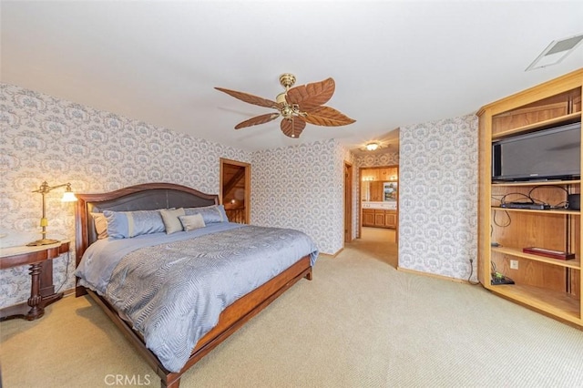 bedroom with light colored carpet, ceiling fan, and ensuite bath