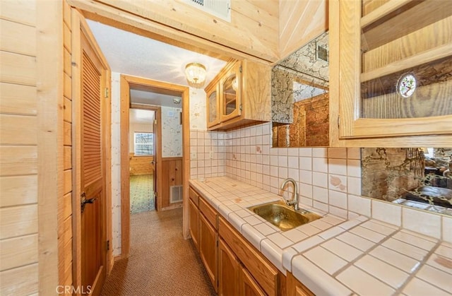 kitchen featuring carpet flooring, wooden walls, tile counters, backsplash, and sink